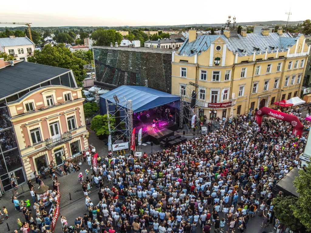 Ludzie zebrani pod sceną podczas Dni Chełma, widok z góry. W centralnym punkcie scena z oświetleniem, obok budynek magistratu.