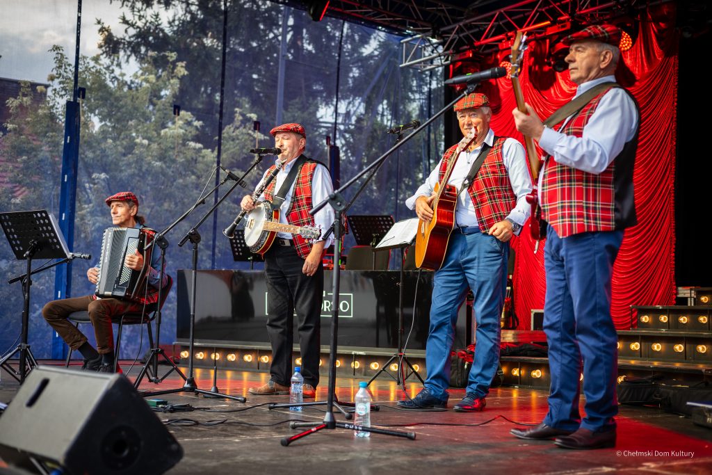 Zespół w kraciastych kamizelkach gra na instrumentach: akordeon, banjo, gitara, bas.